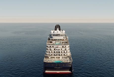 A Greek Isle explora large cruise ship sails on a calm ocean under a clear blue sky. The ship's decks are visible from the rear, with a pool on the lower deck.