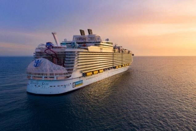 A Royal Caribbean Cruise large cruise ship, Wonder of the Seas, sails on calm ocean waters under a vibrant sunset sky, creating a serene and majestic ambiance.