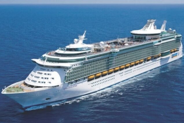 A Royal Caribbean Cruises large white cruise ship sails smoothly on a vast, calm ocean under a clear blue sky, conveying a sense of adventure and tranquility.