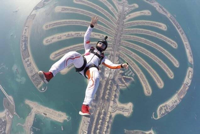 Skydiver in a white suit with red accents freefalls above Dubai’s Palm Jumeirah, capturing a thrilling moment with an aerial view of the iconic island.
