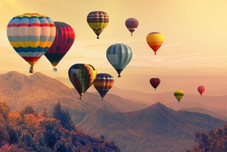 A group of colorful hot air balloons floats above scenic mountains in a warm, golden sunset in UAE. The scene is peaceful and vibrant, evoking a sense of adventure.