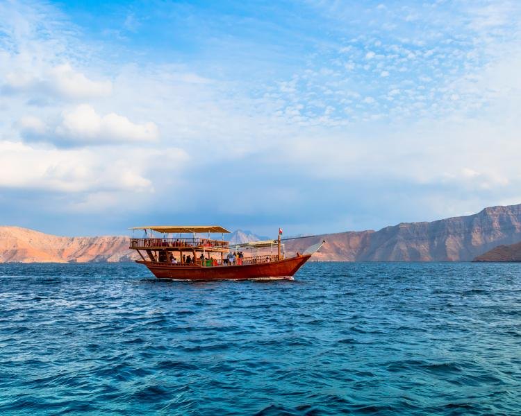 Tour boat cruising through the fjords of Musandam with rugged mountains in the background