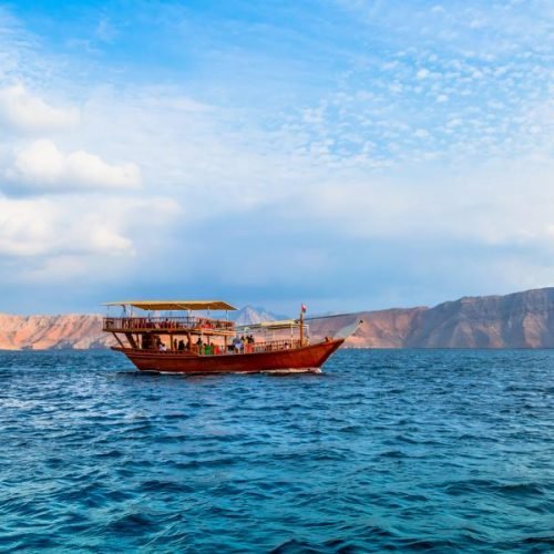 Tour boat cruising through the fjords of Musandam with rugged mountains in the background